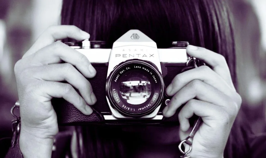 Fotografin hält eine analoge Kamera vor das Gesicht (KI-generiert)